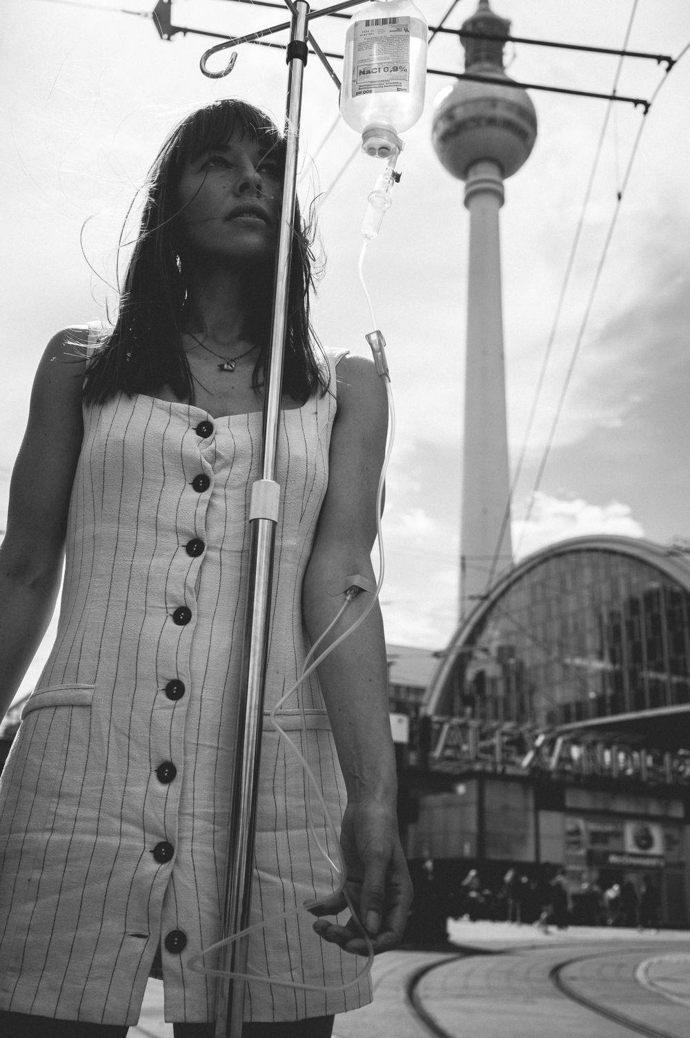 Black and white street scene in Berlin with a white dress, IV pole, and the TV Tower and Alexanderplatz station visible.