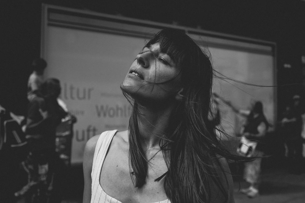 A dramatic black and white portrait of someone in a white tank top with long dark hair looking upward in deep thought.