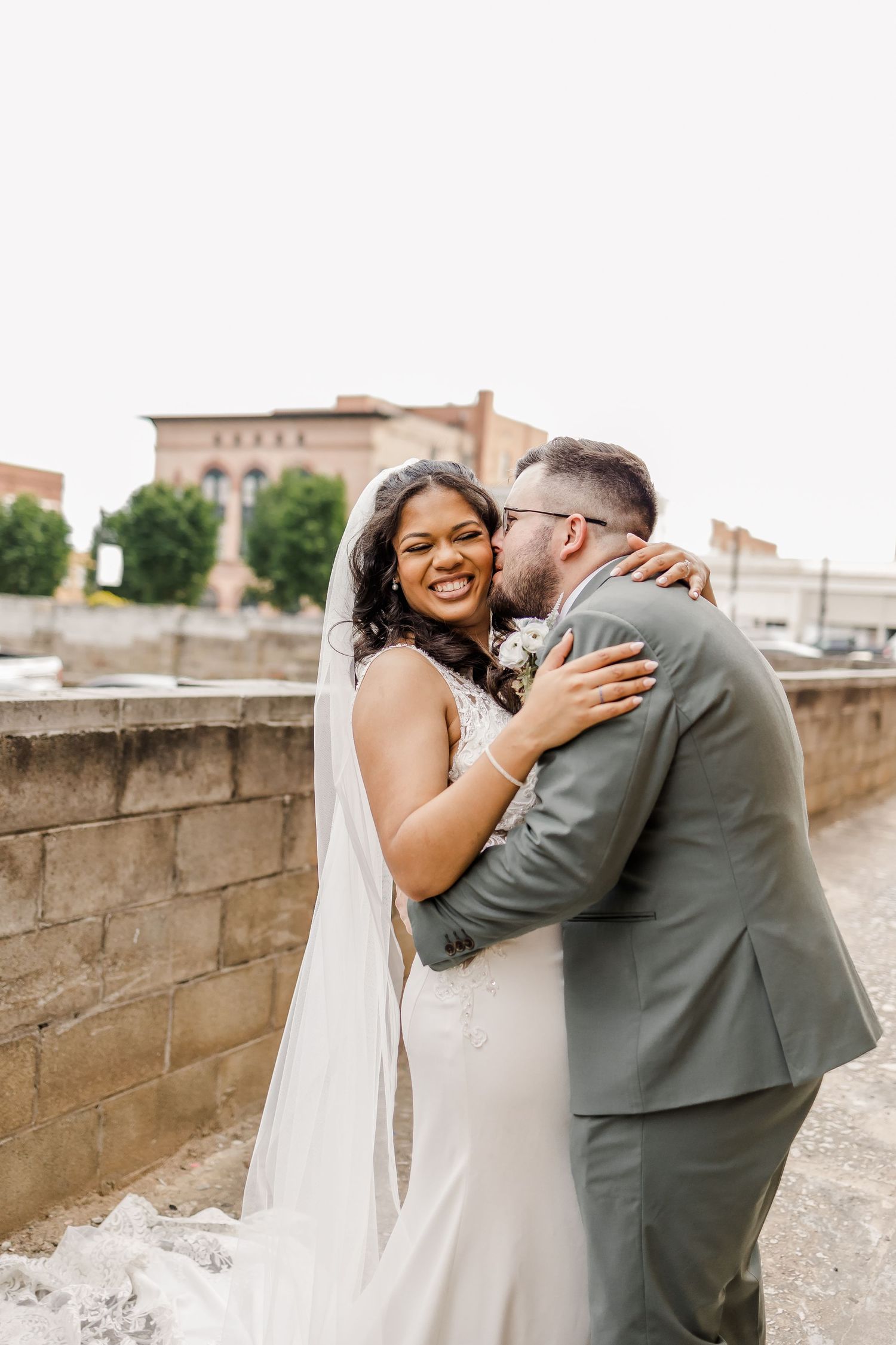 Newlyweds share a tender moment against stone wall backdrop.