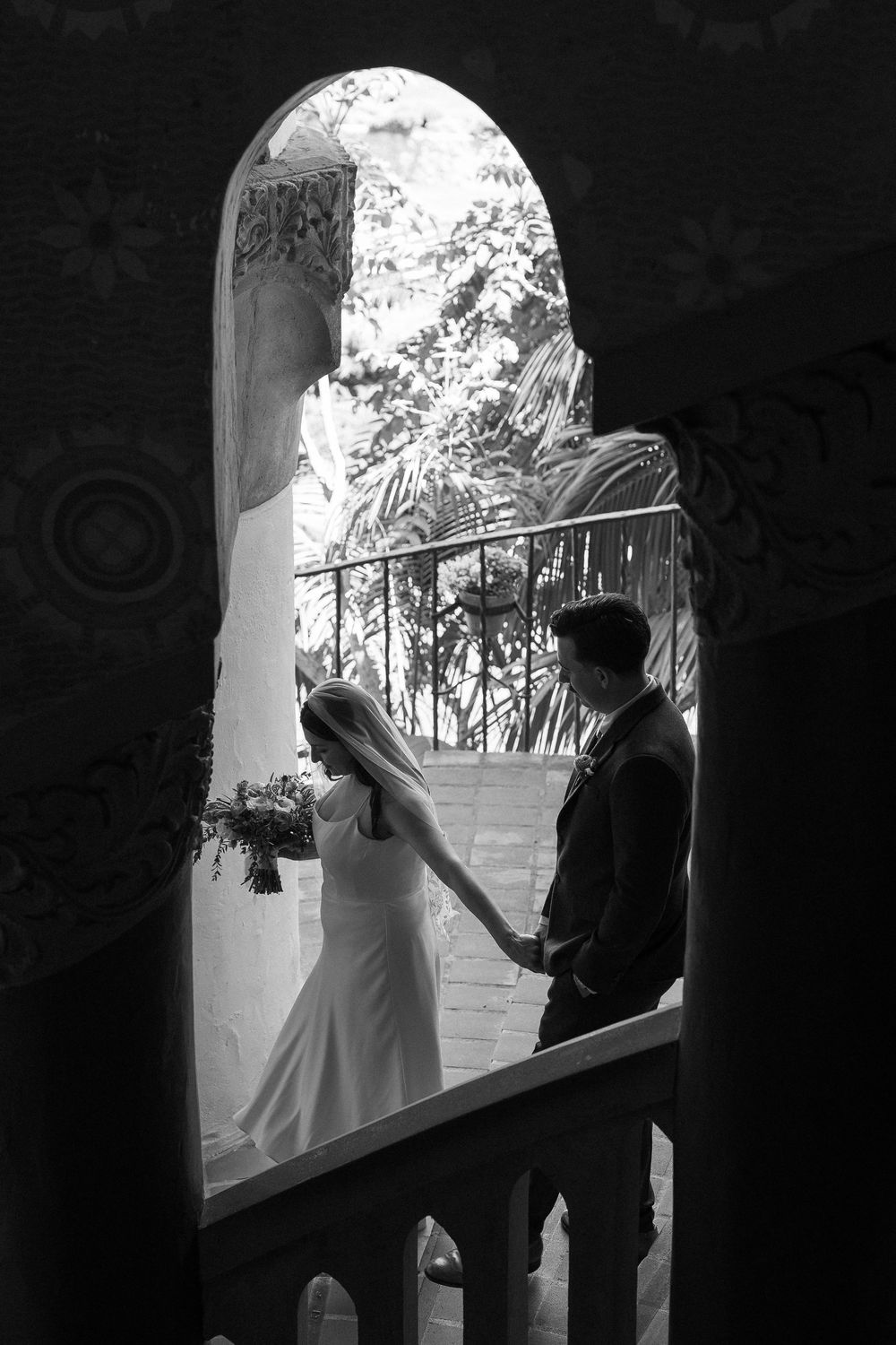 Black and white film photo of couple walking through tiled hallway.