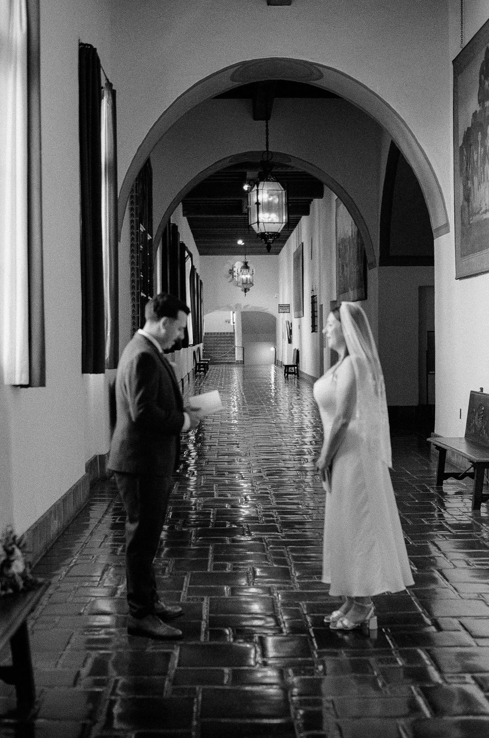 Black and white film photo of couple embracing under courthouse archway.