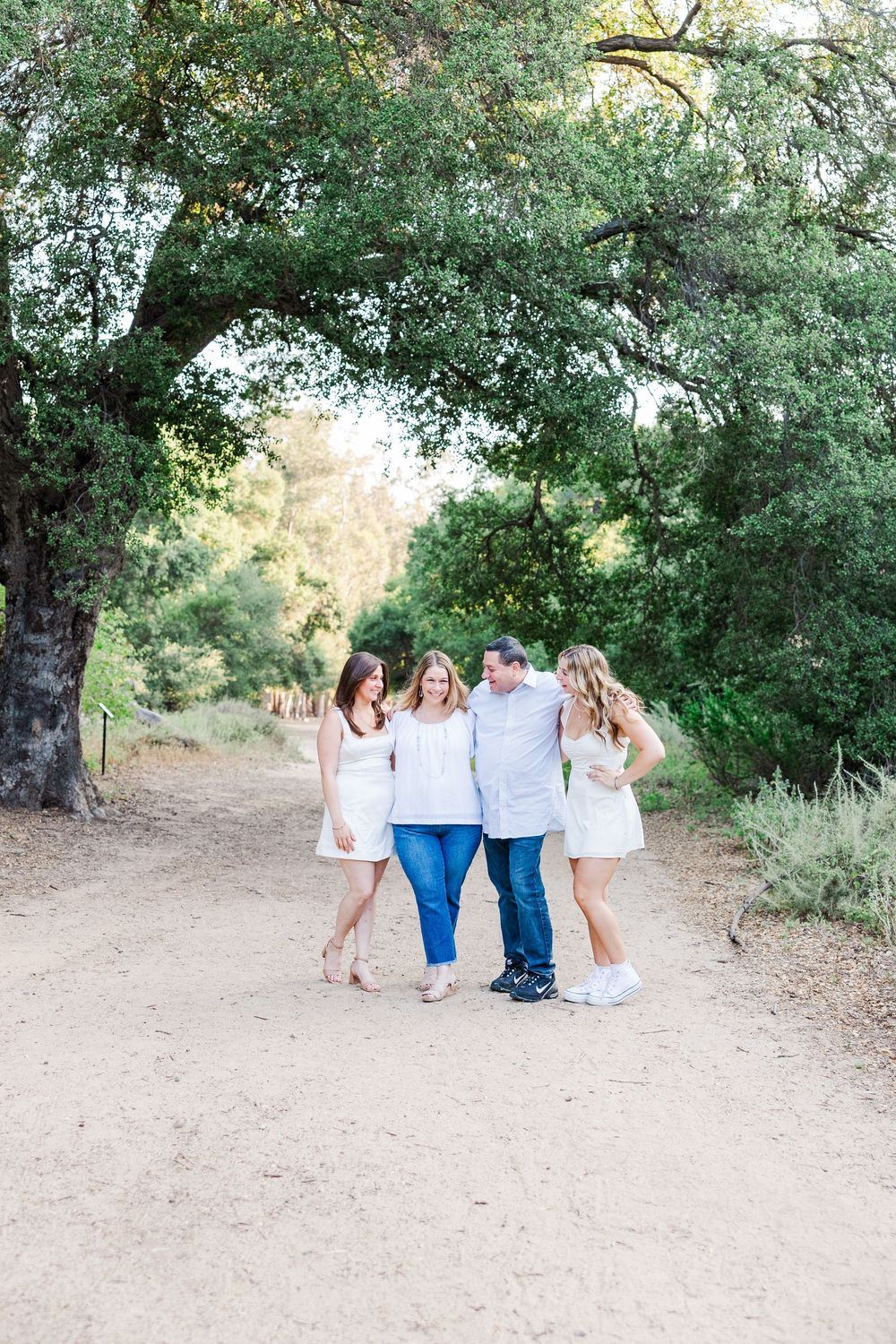 A group walking together along a dirt trail surrounded by lush green trees on a bright sunny day.