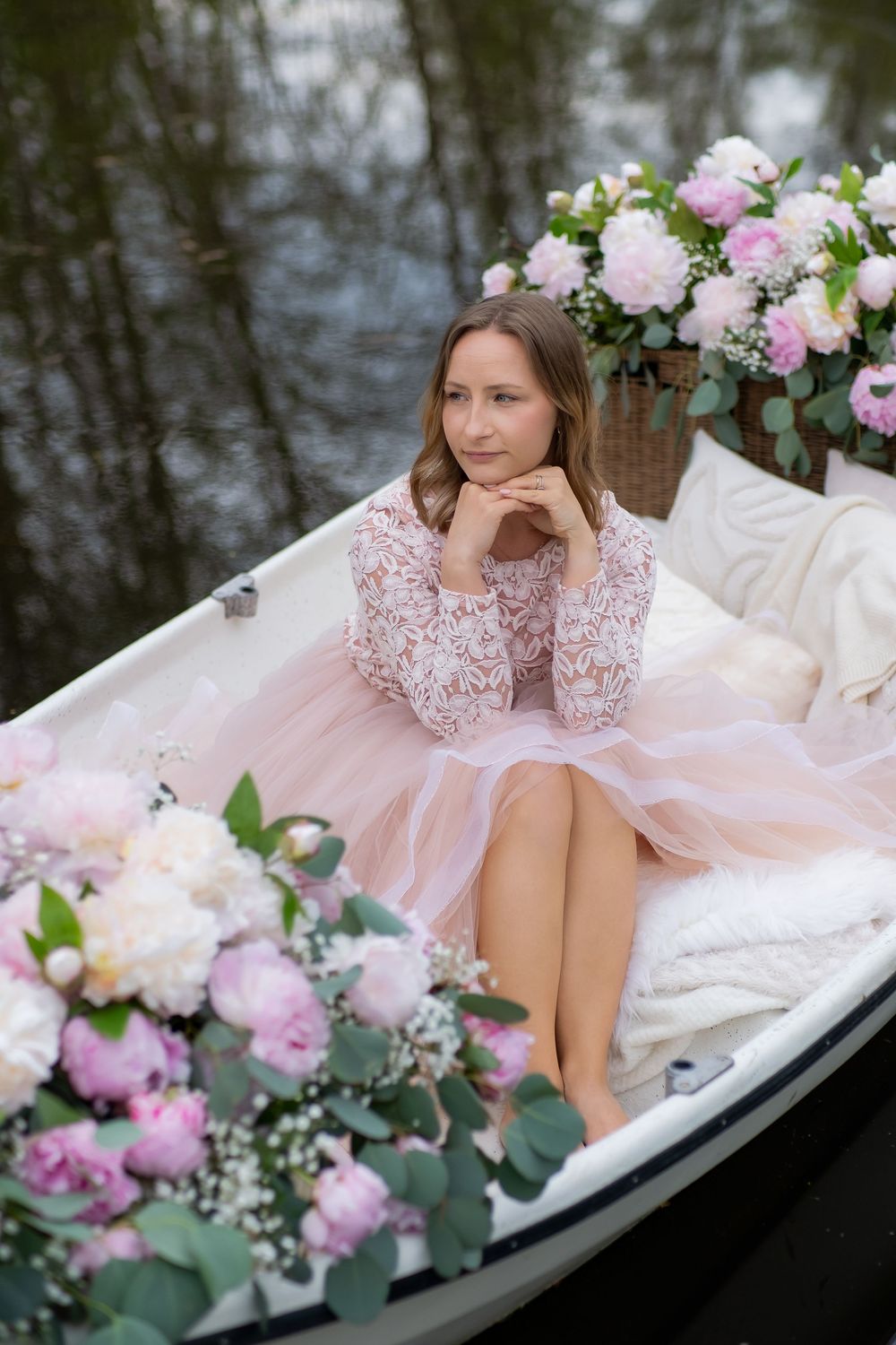 Romantic scene in rowboat decorated with pink and white peonies and cushions on tranquil water.