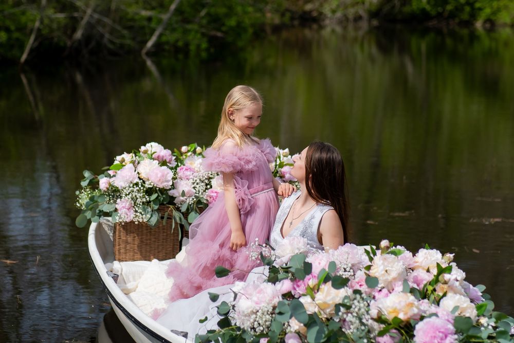 Two people sit in a white boat decorated with pink and white floral arrangements on calm water.