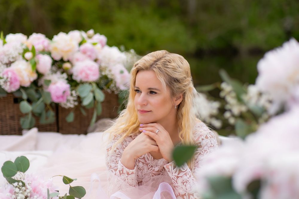 Elegant woman in pink lace dress sits at romantic outdoor table decorated with pink peonies and eucalyptus.