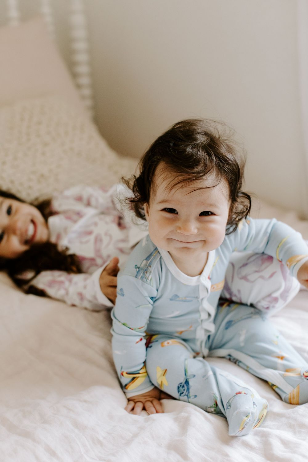 Baby in light blue pajamas lying on white bedding with a sweet smile.