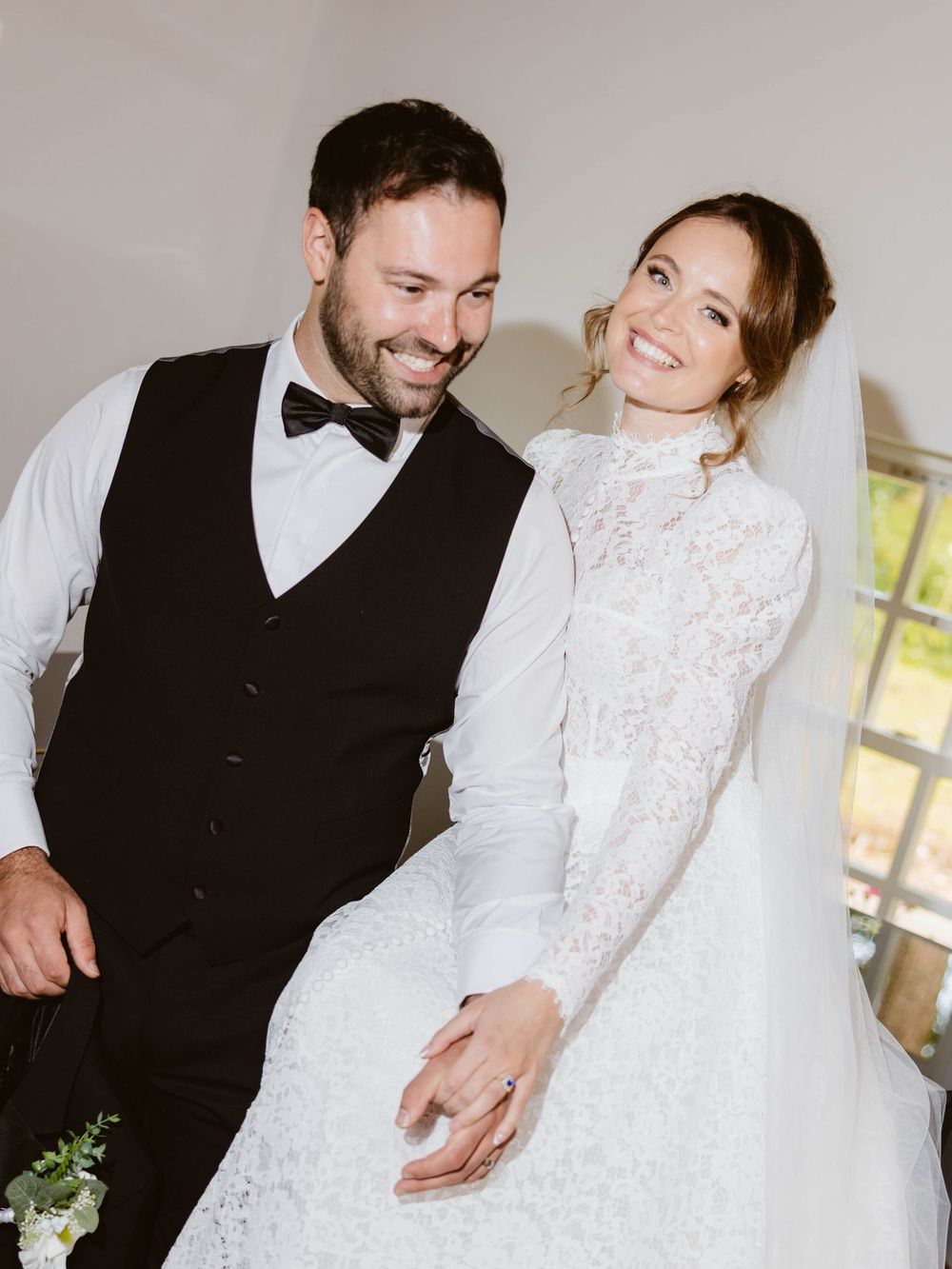 A happy couple shares a candid moment together on their wedding day, dressed in formal black tie and white lace attire.