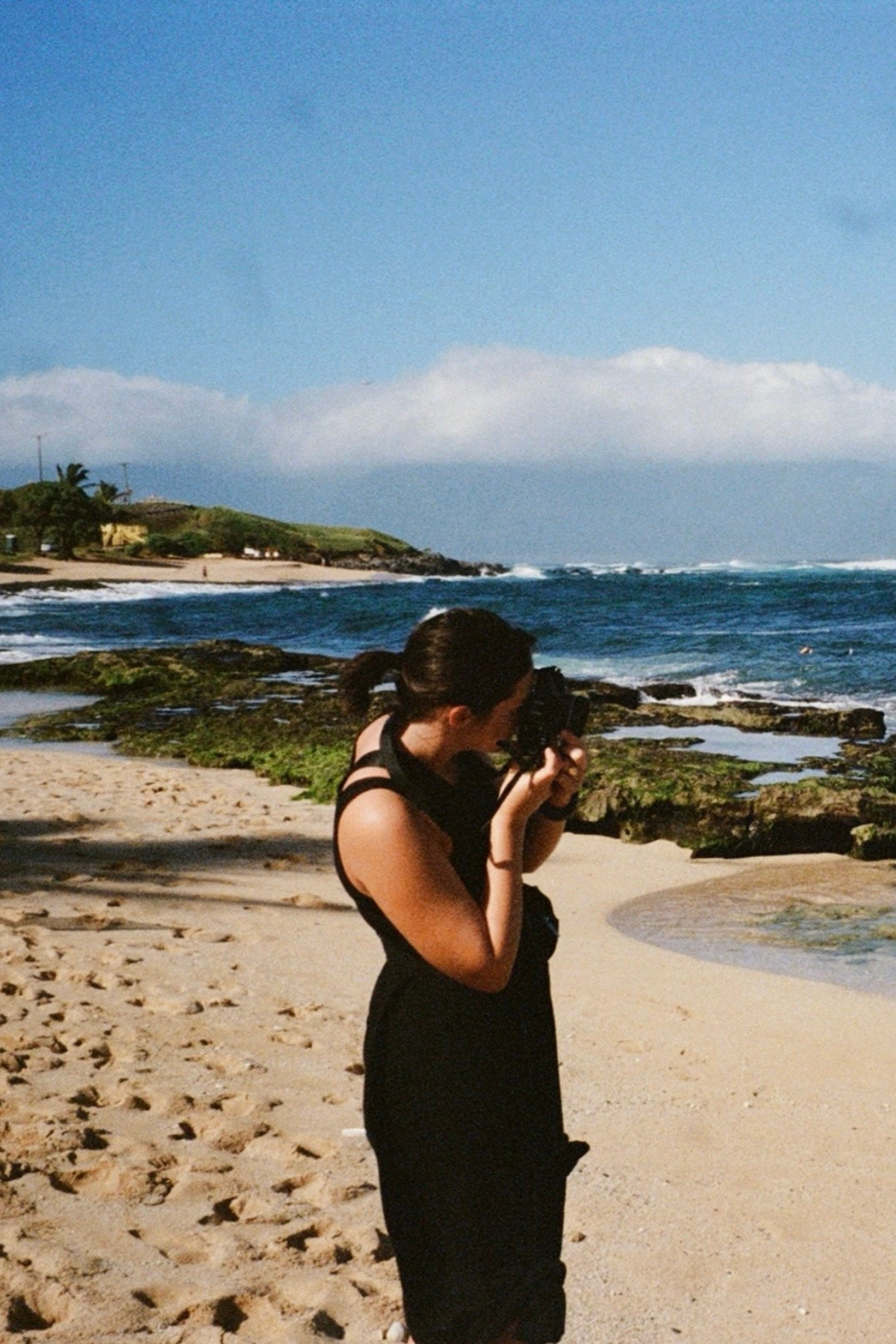 Photographer captures ocean scenery from sandy beach with rocky coastline.
