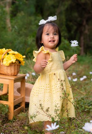 Cute toddler girl in yellow dress holding white daisy flower in a garden setting outdoors.