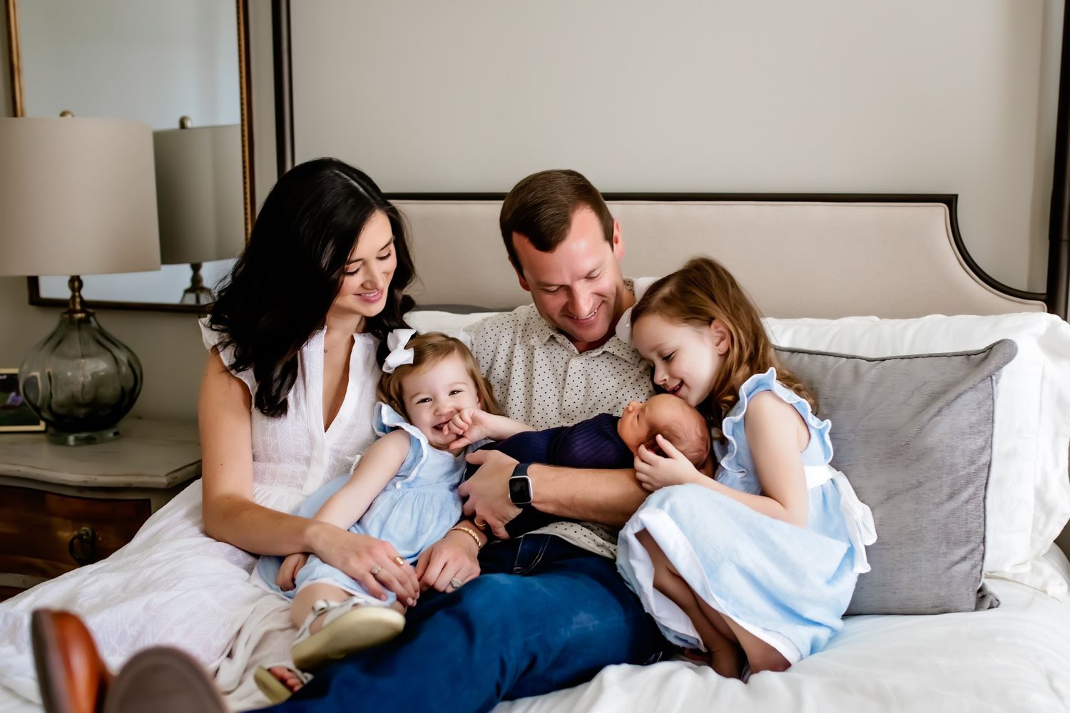 A family relaxes together on a white bed while sharing tender moments in a series of connected photographs.