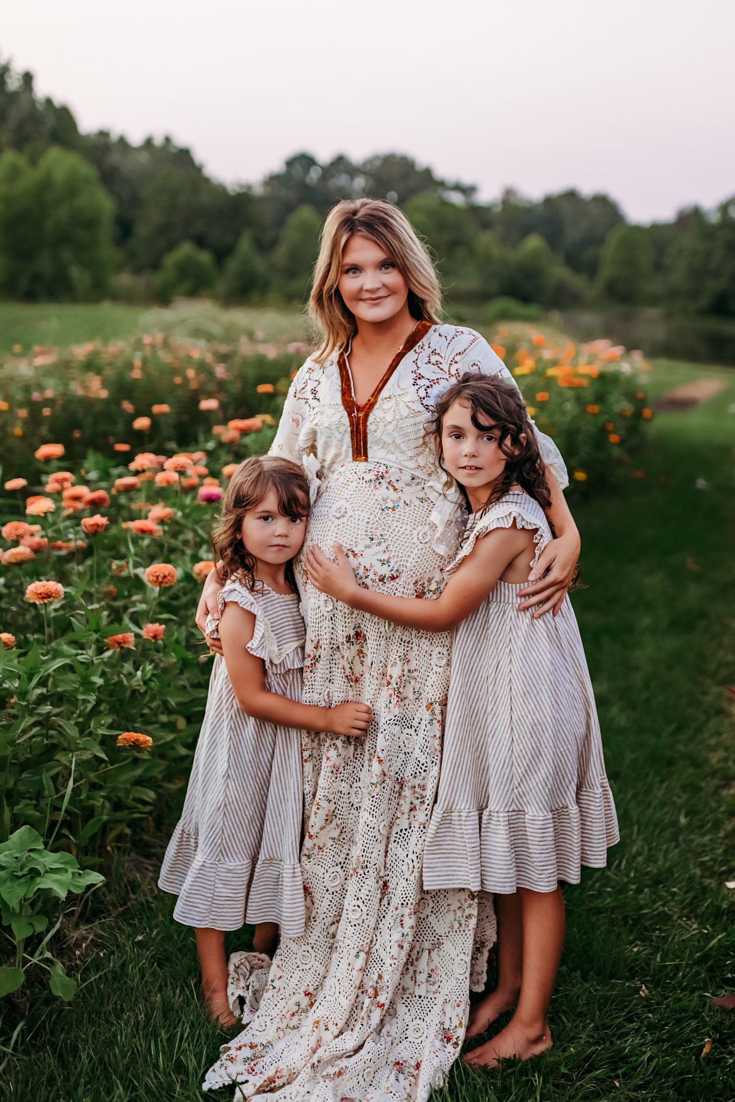 A family wearing white and cream colored dresses poses together in a garden of orange flowers at sunset.