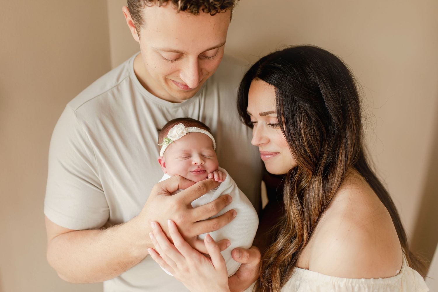 New parents smile adoringly at their swaddled newborn baby girl during a professional studio portrait session.