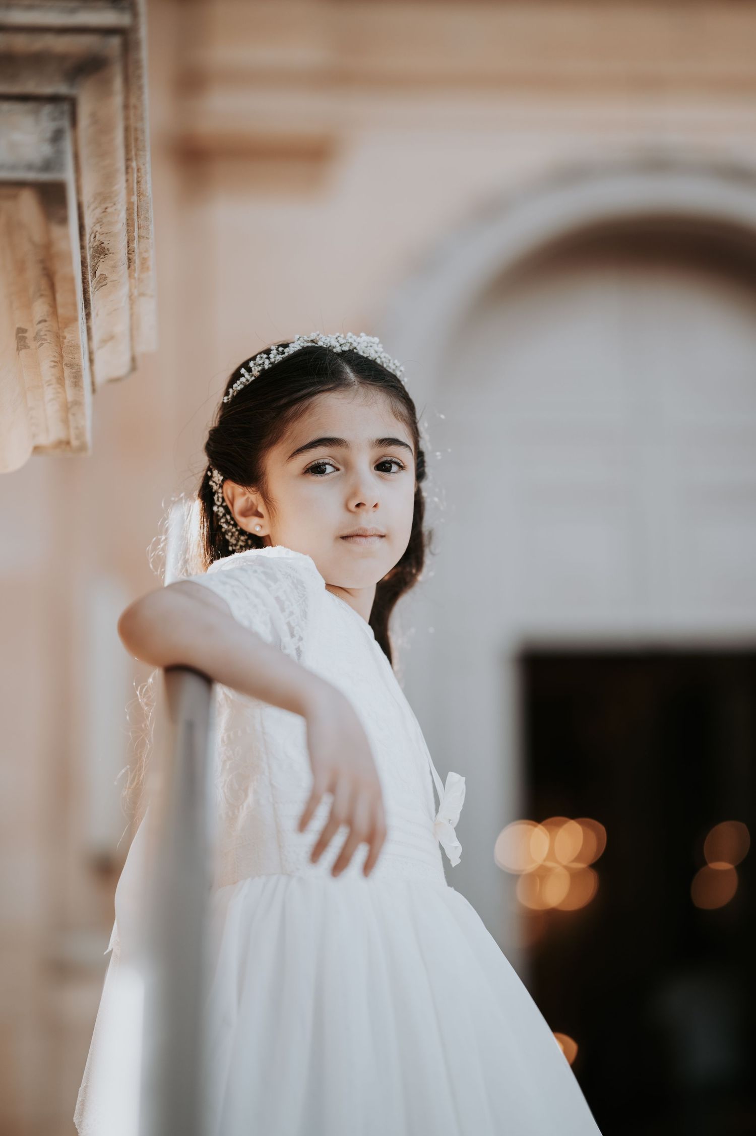 Person in white dress leaning against stone column in soft lighting.