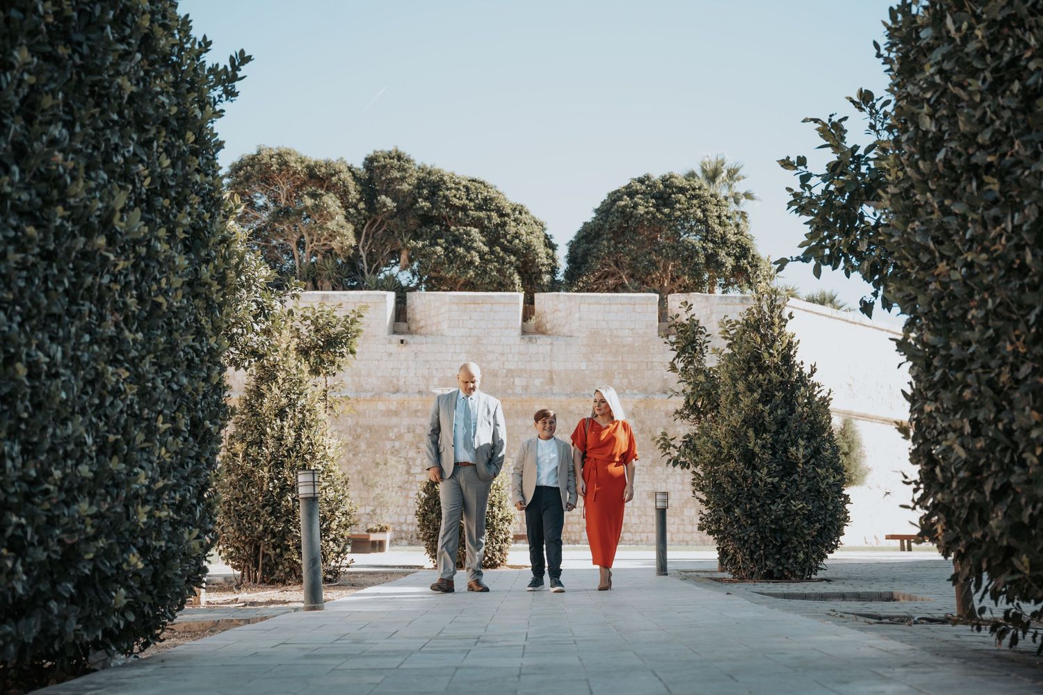 Wide landscape shot of people walking together on a path surrounded by manicured shrubs.