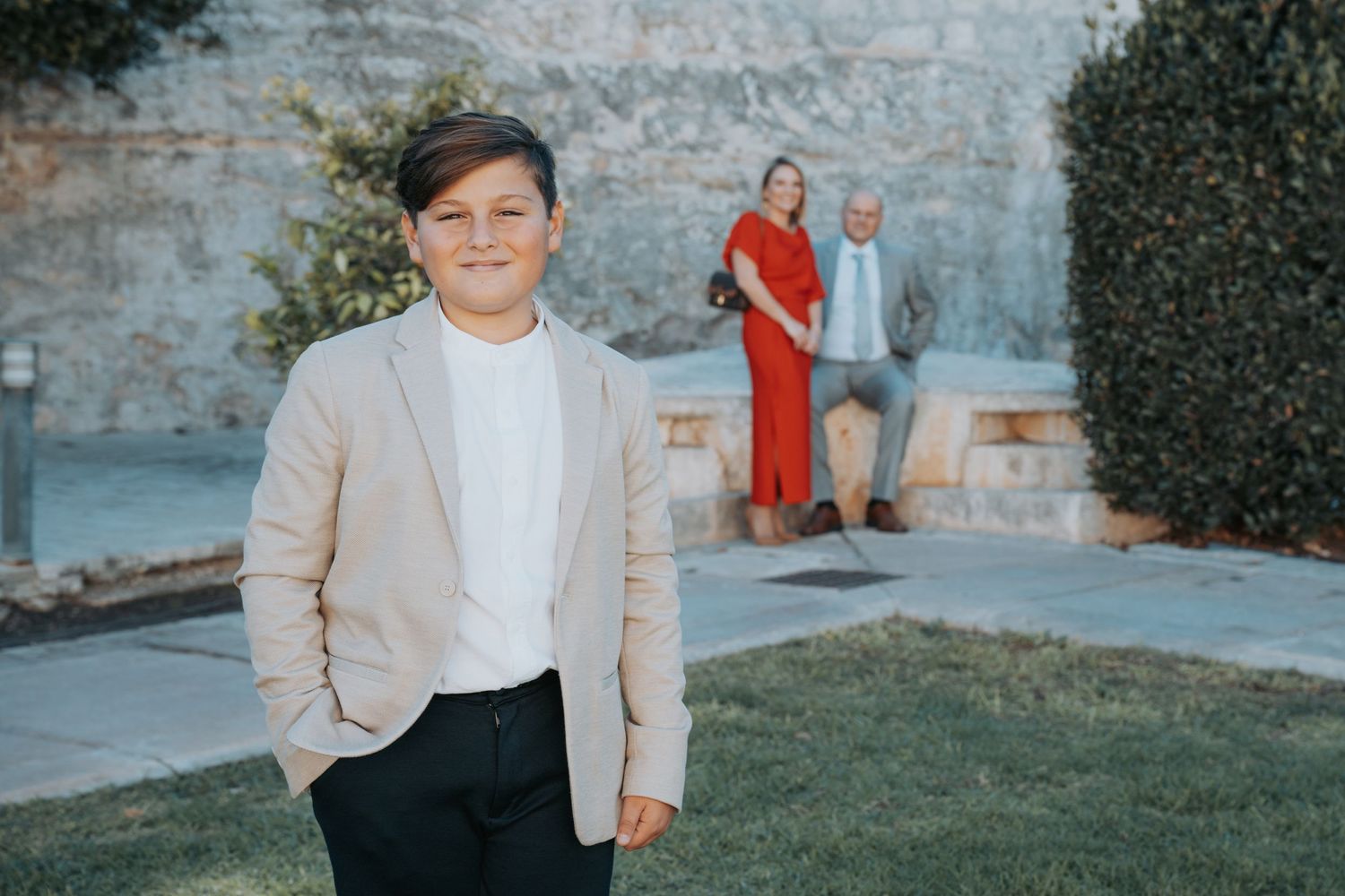 A casual outdoor family photoshoot with stone walls and greenery in the background.