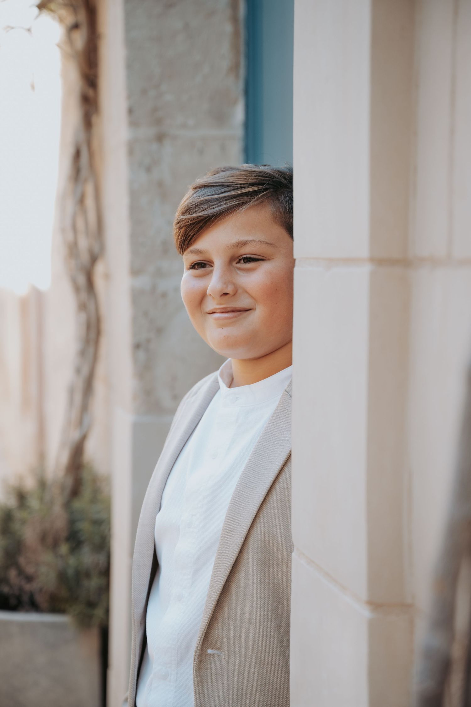 A stylish portrait against white columns showing someone in a light colored suit and white shirt.