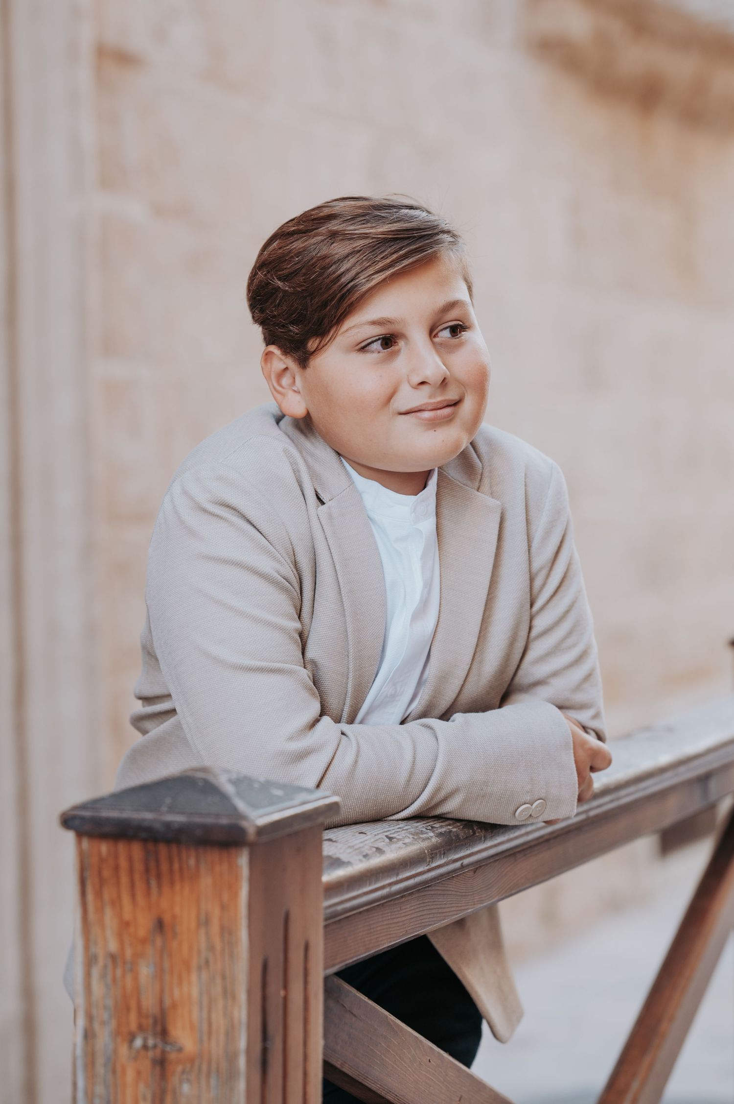 A young person in a light blazer leans on a wooden railing in a contemplative pose.
