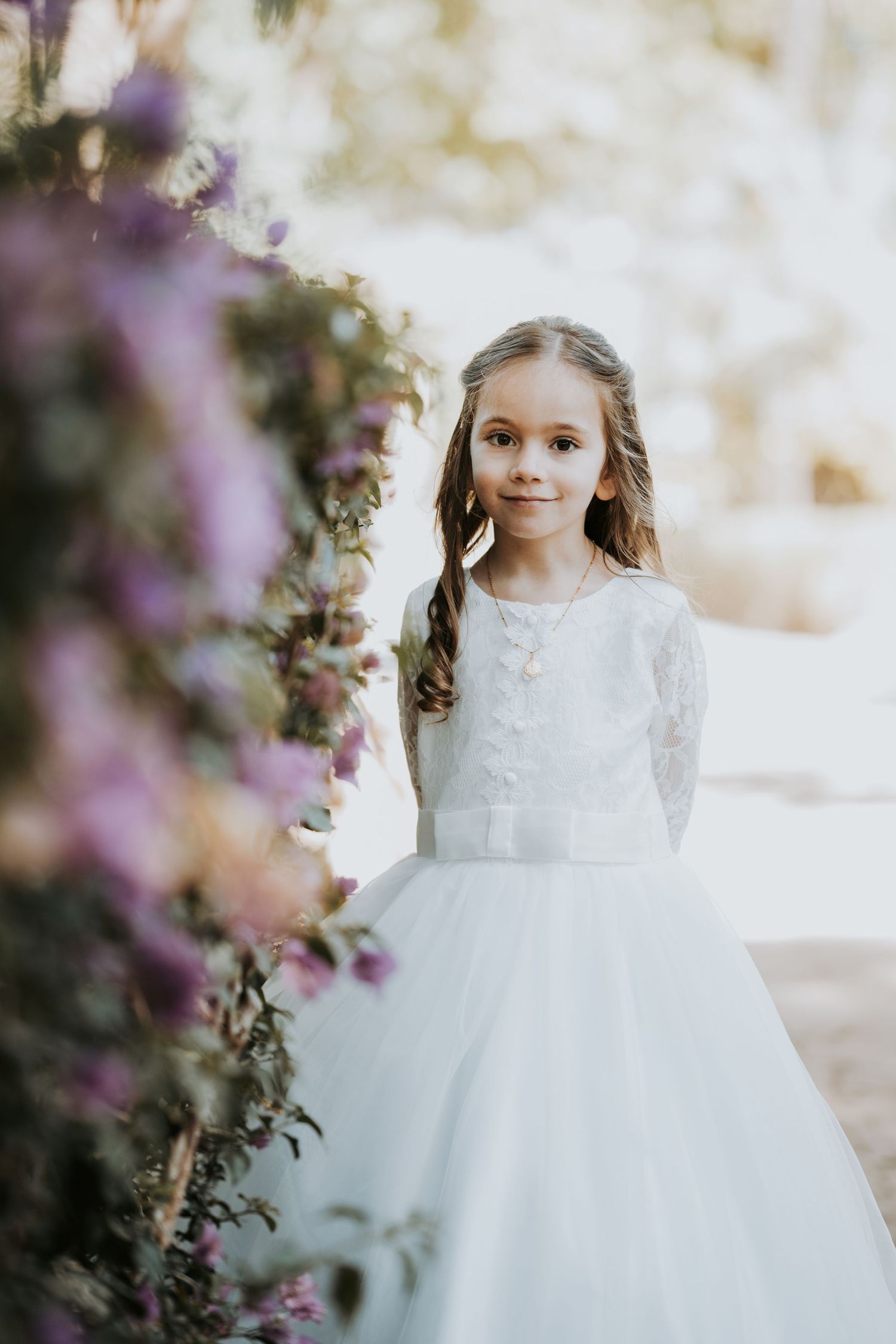 Elegant portrait among purple flowers wearing white ceremonial dress.