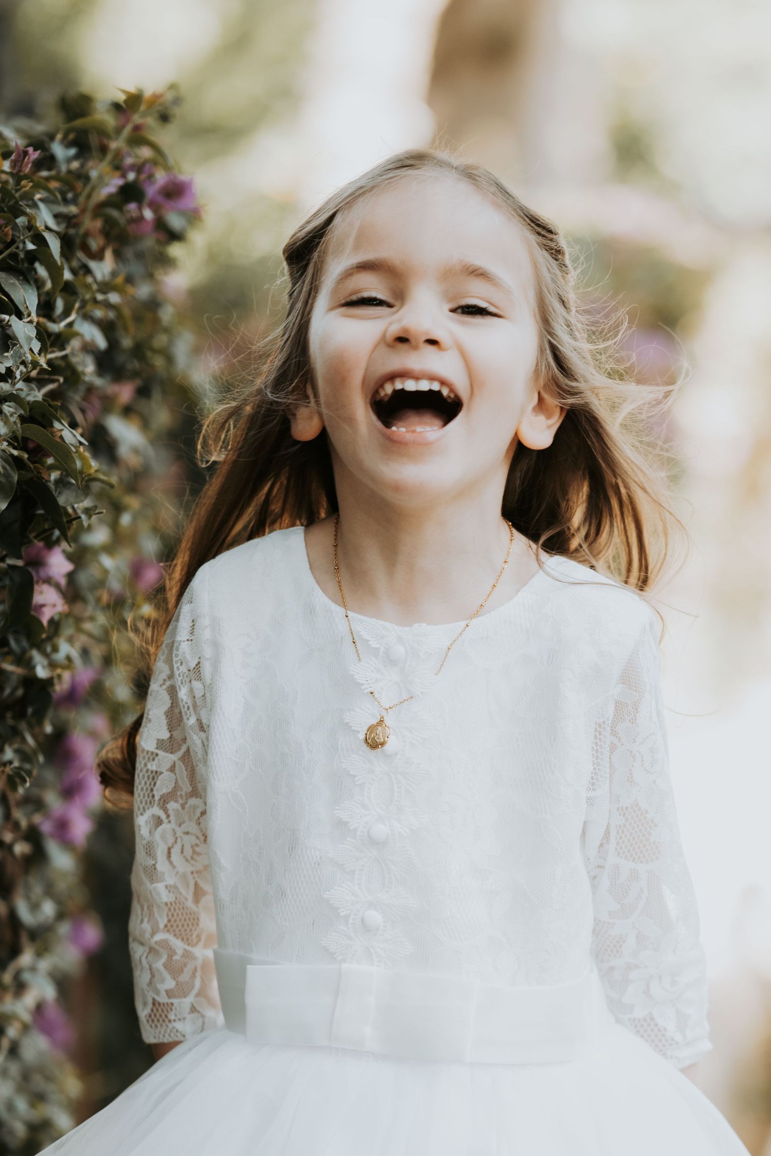 Joyful moment captured in garden setting with flowering bushes and white lace dress.