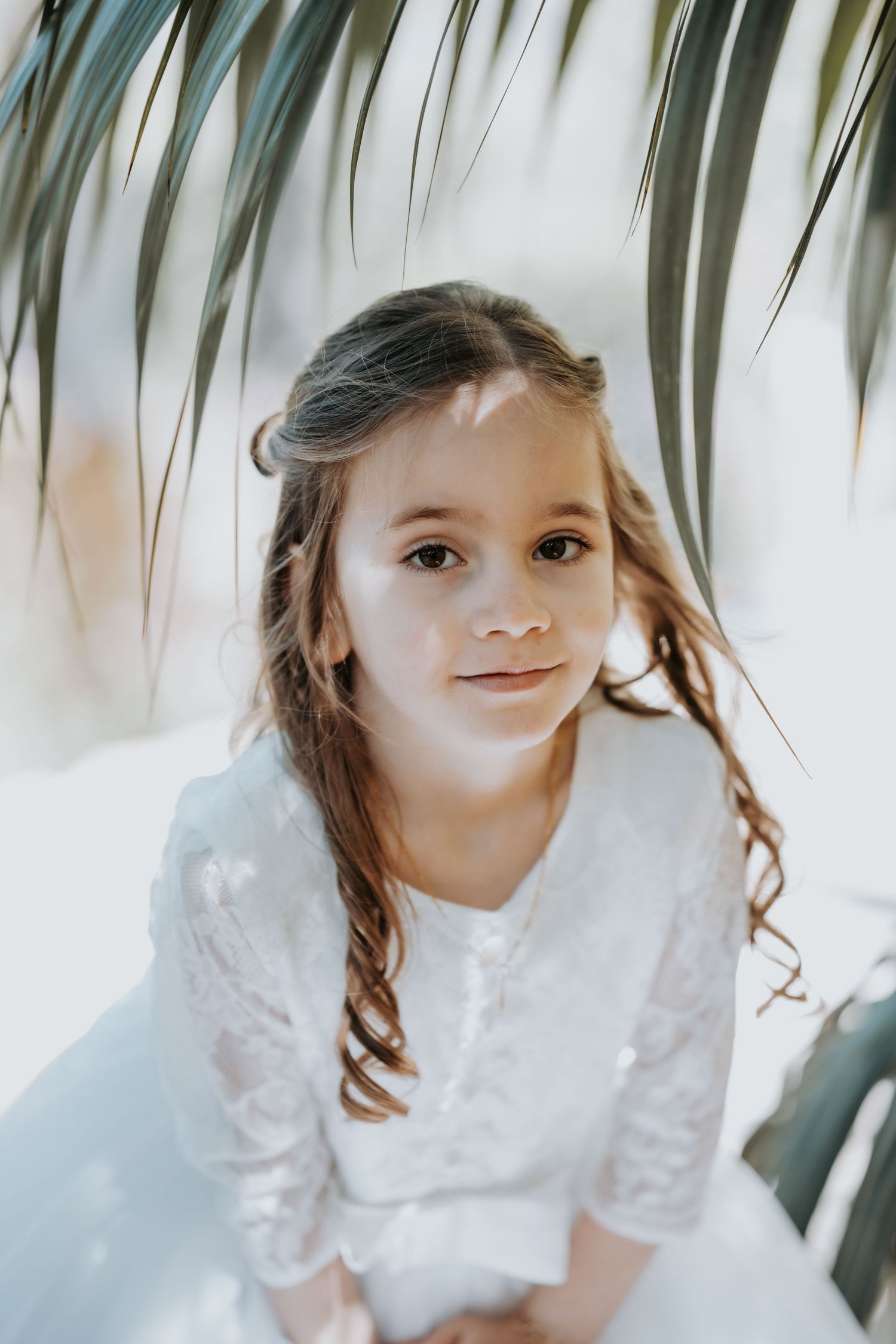 Close-up portrait under palm fronds showing white lace dress details.