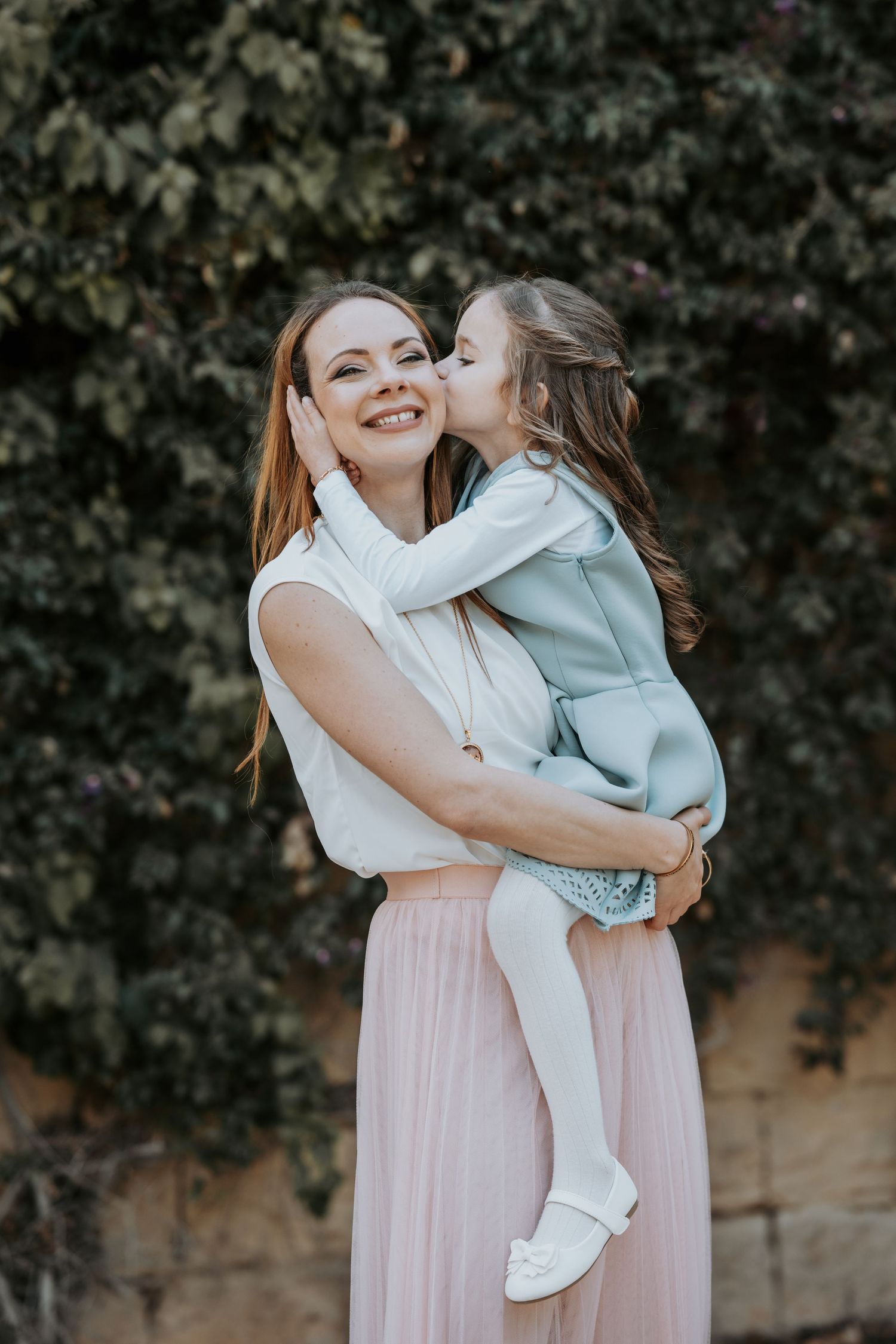 Mother and child sharing tender moment outdoors while wearing pink and light blue outfits.