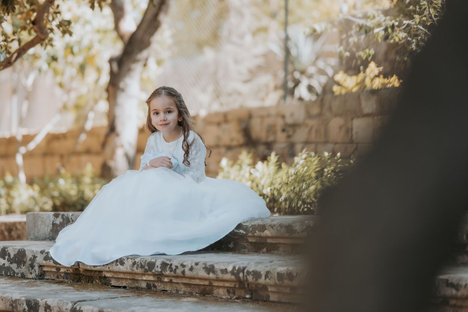 Sun-dappled garden scene with stone walls and flowing white dress creating romantic atmosphere.