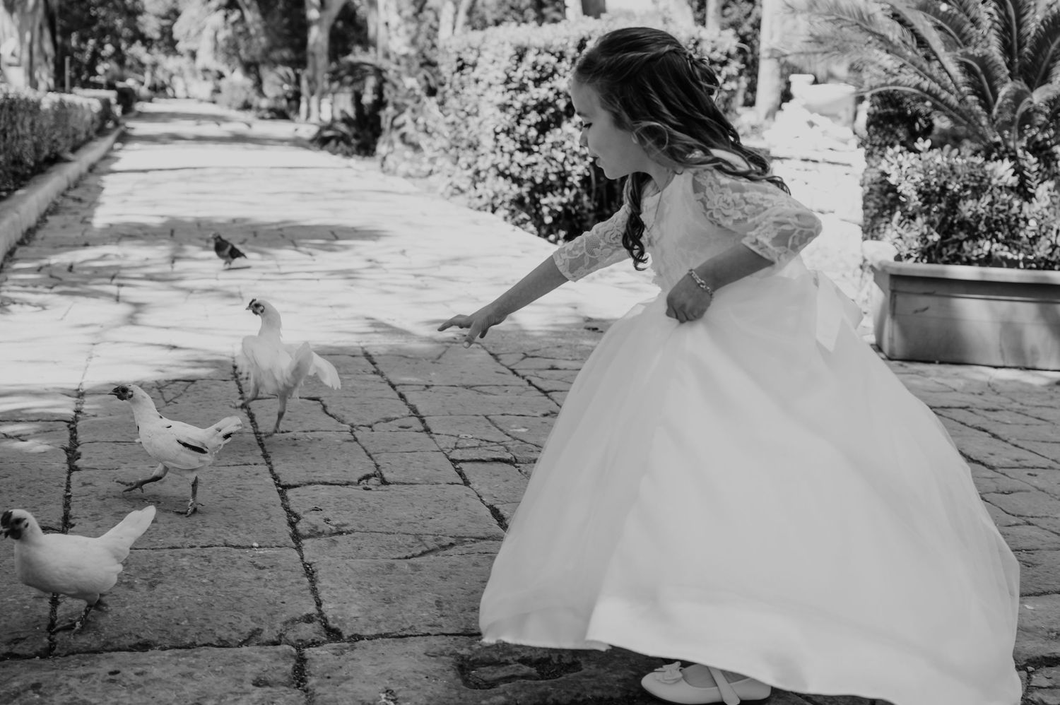 Child in flowing white dress sitting gracefully on stone steps in an outdoor garden setting.