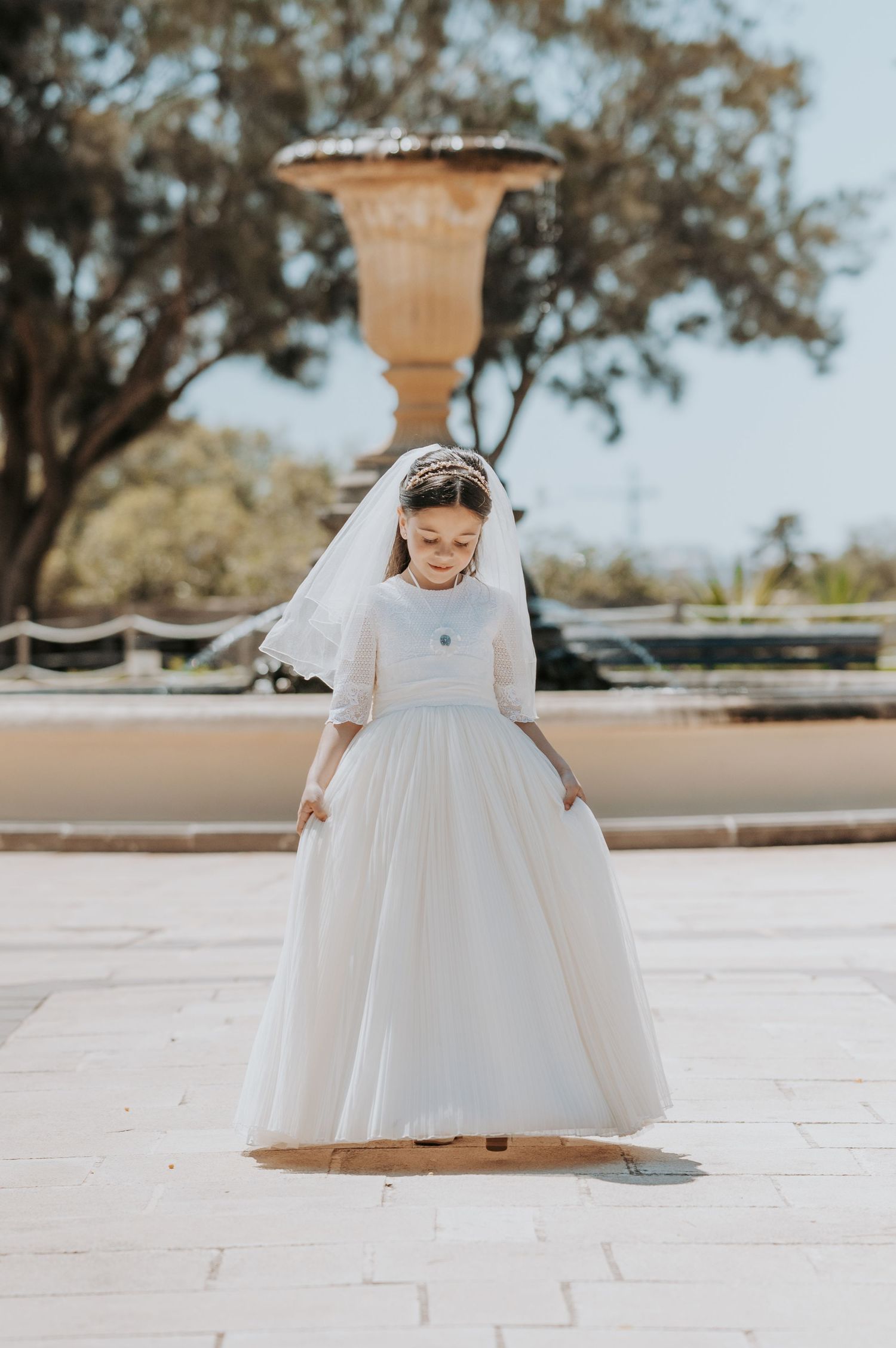 A young person in a white formal dress twirling on a stone patio surrounded by trees.