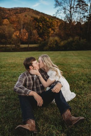 A couple shares an intimate moment on grass with autumn foliage in the background.