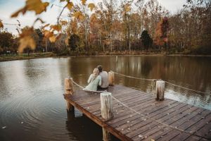A wooden dock extends into a peaceful lake surrounded by autumn trees.