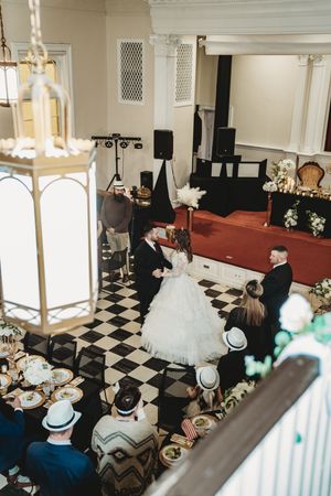 Aerial view of a wedding ceremony on black and white checkered floor with bride and groom exchanging vows.
