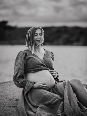 A series of black and white maternity photos showing a pregnant person reclining outdoors in a casual dress.