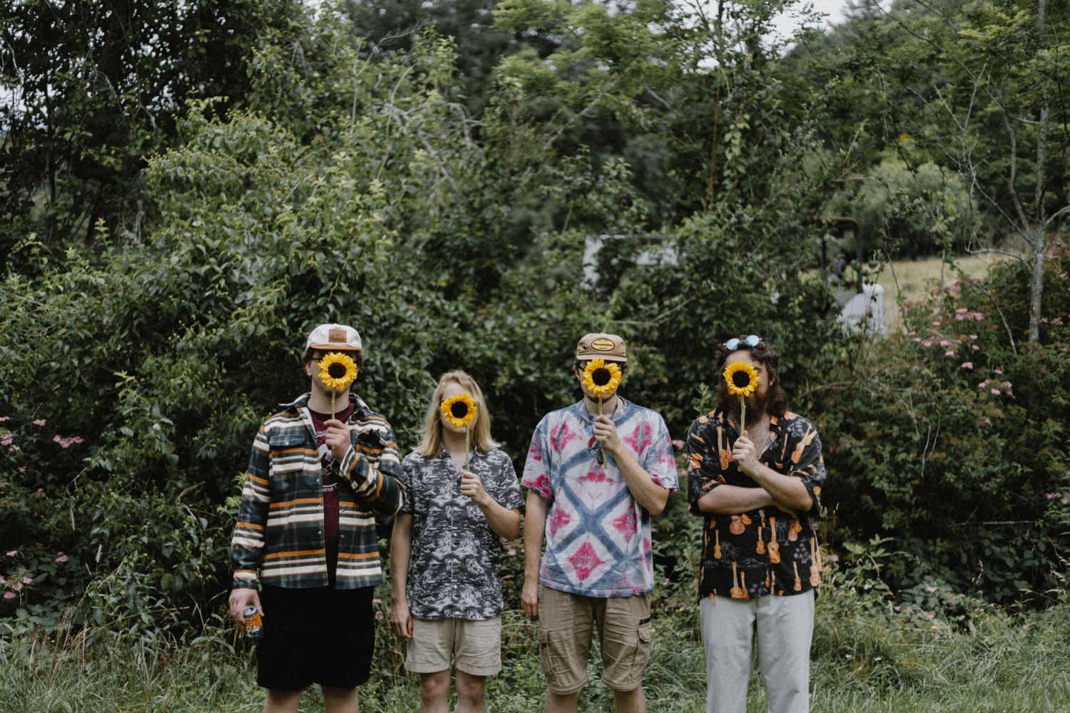 Four people wearing sunflower masks standing together in green outdoor setting.
