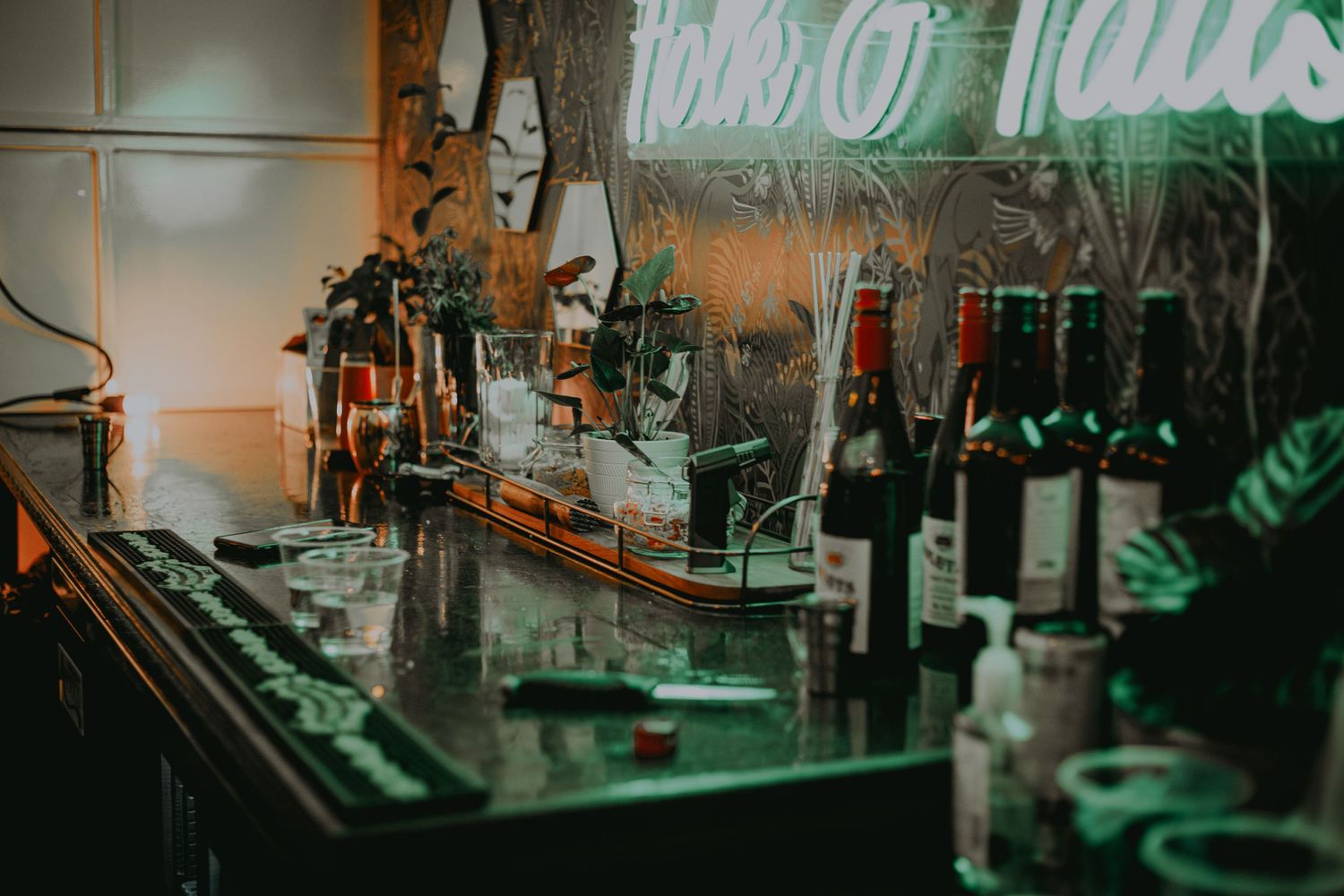 Dimly lit bar counter with liquor bottles and taps in atmospheric green lighting.