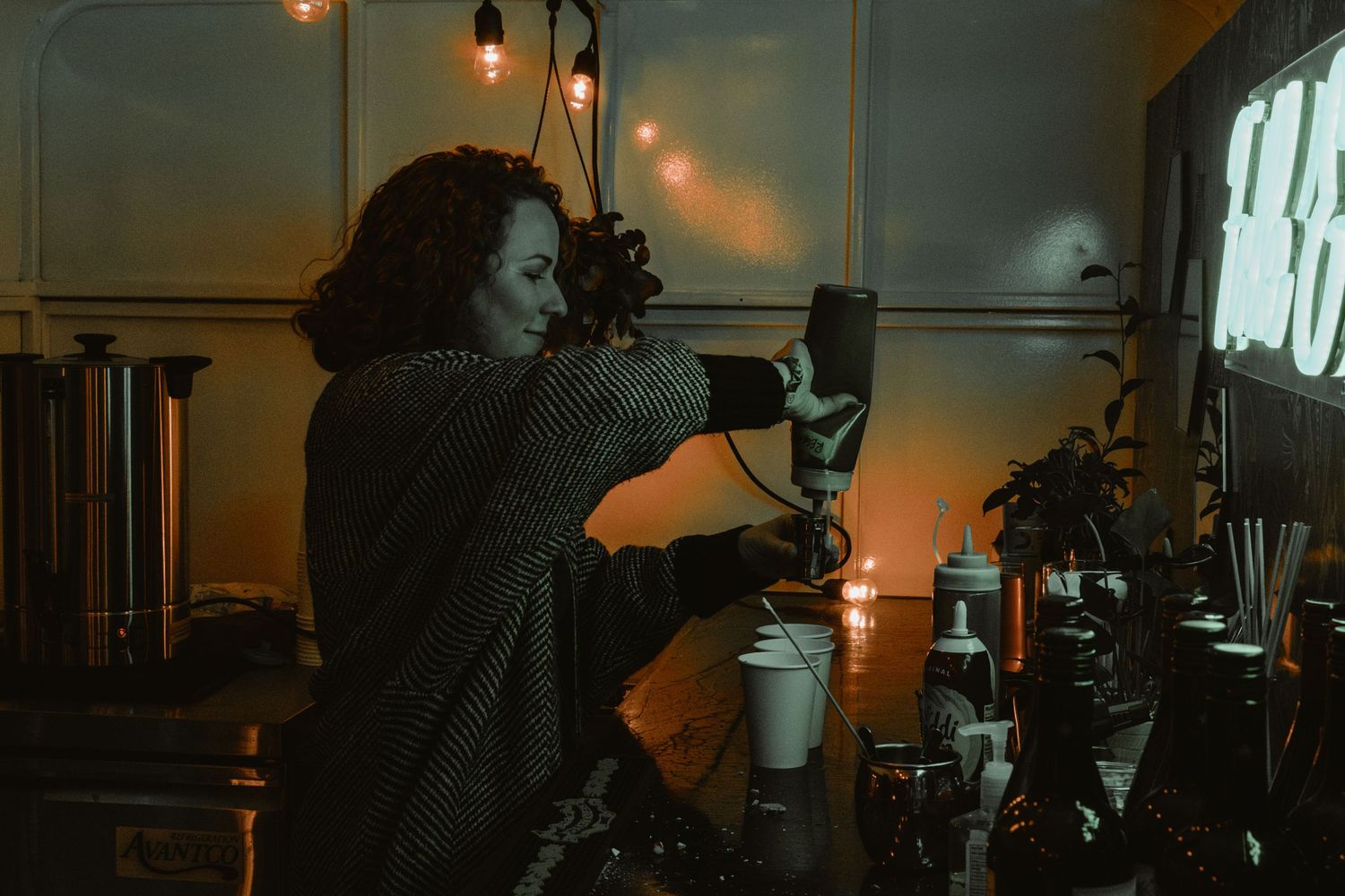 Someone photographs coffee preparation with professional camera equipment in moody lighting.