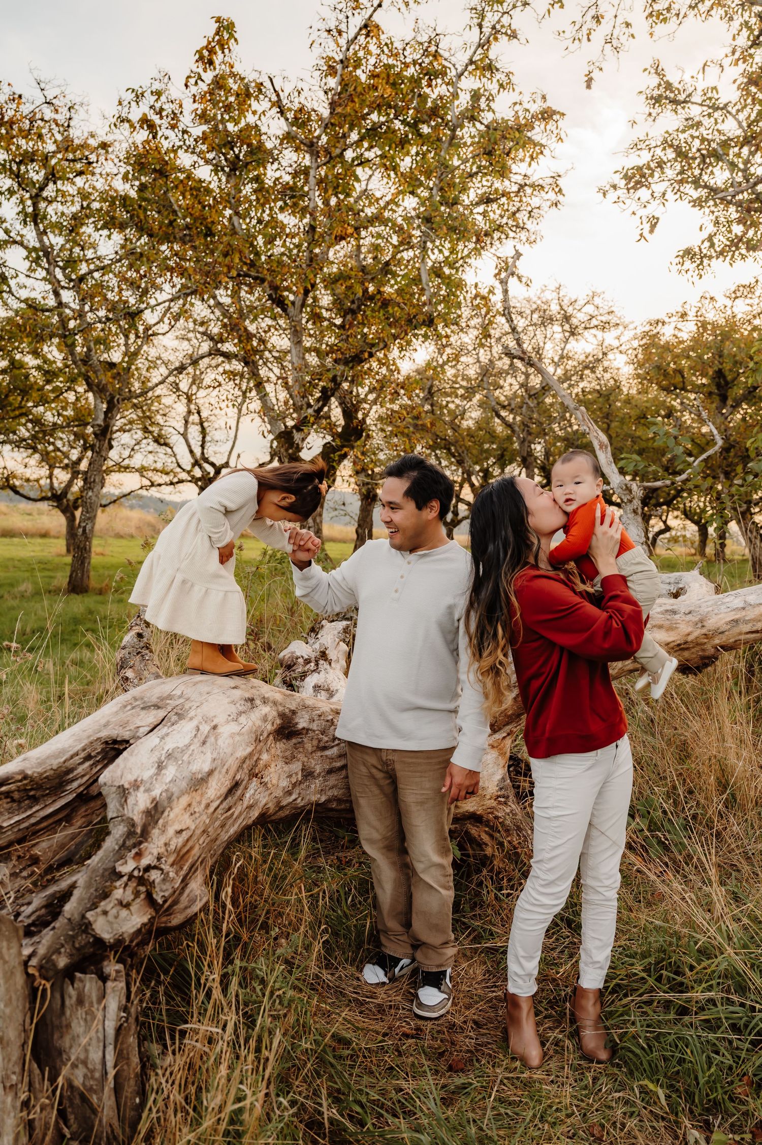 Family of four stands together by a log