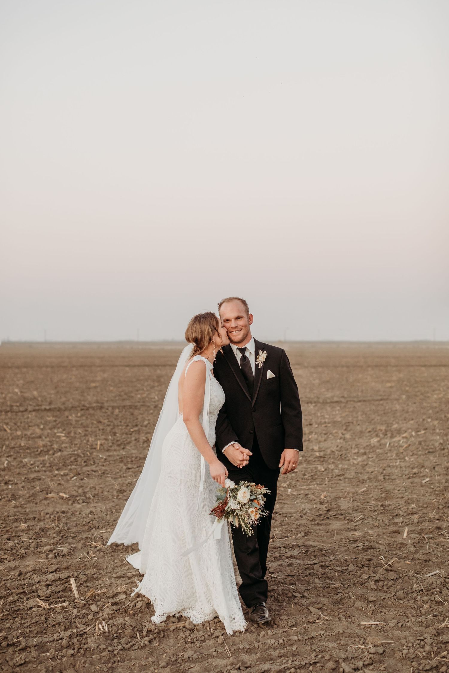 Newlyweds share intimate moment in open field during sunset.