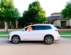 White luxury SUV parked in front of a residential home with green trees in the background.