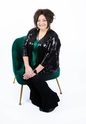 A person in a black sequin jacket and emerald green dress poses in different positions on a modern chair against white.