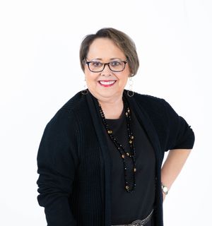 Professional wearing glasses and black attire poses with a friendly smile against white background.