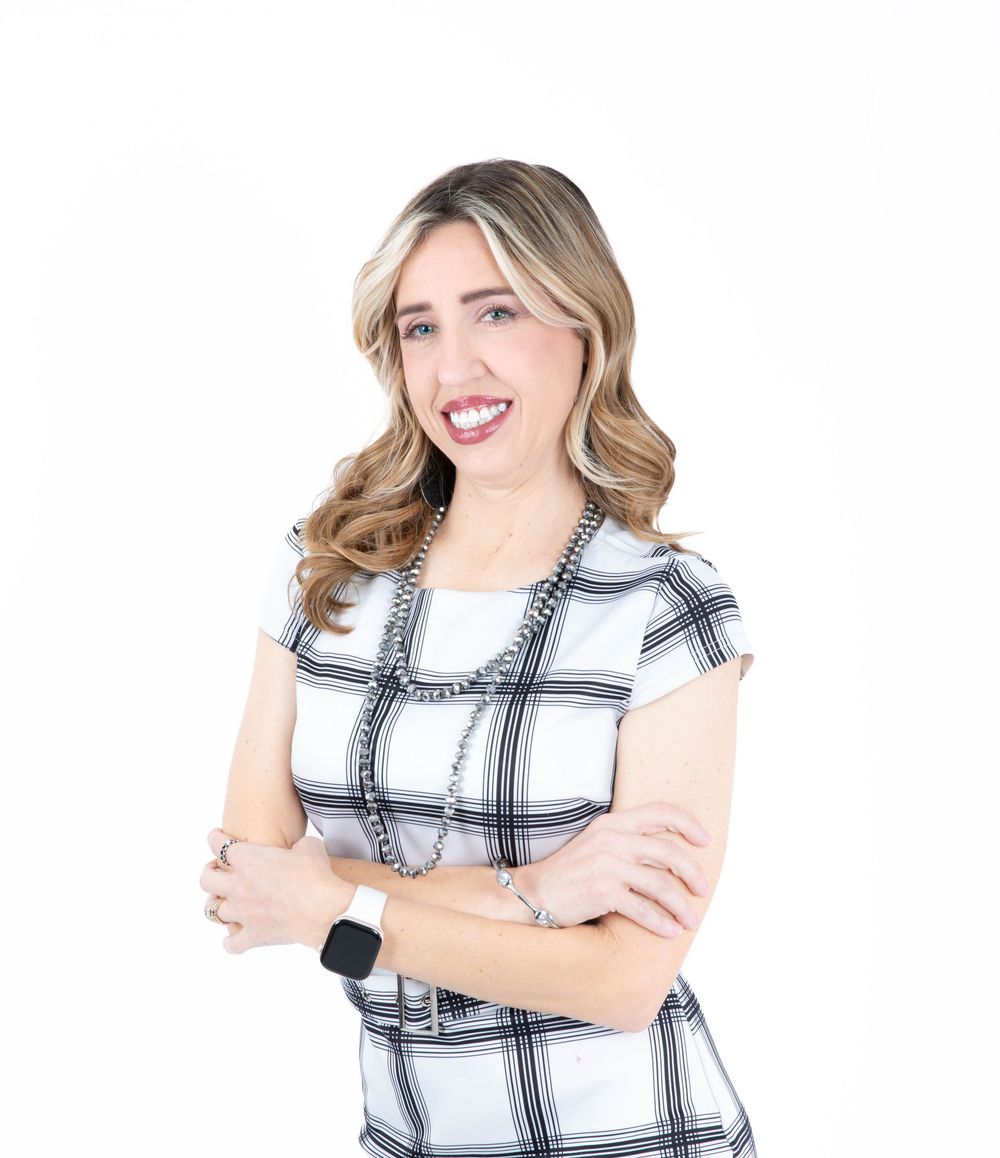 Professional portrait of someone wearing a black and white plaid short sleeve top with arms crossed and a warm smile.