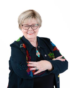 Professional portrait of someone wearing glasses and a black jacket with colorful embroidered details, smiling warmly.