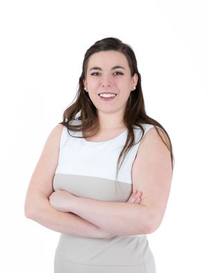 Professional portrait of someone in a white and beige sleeveless top with arms crossed and a warm smile.