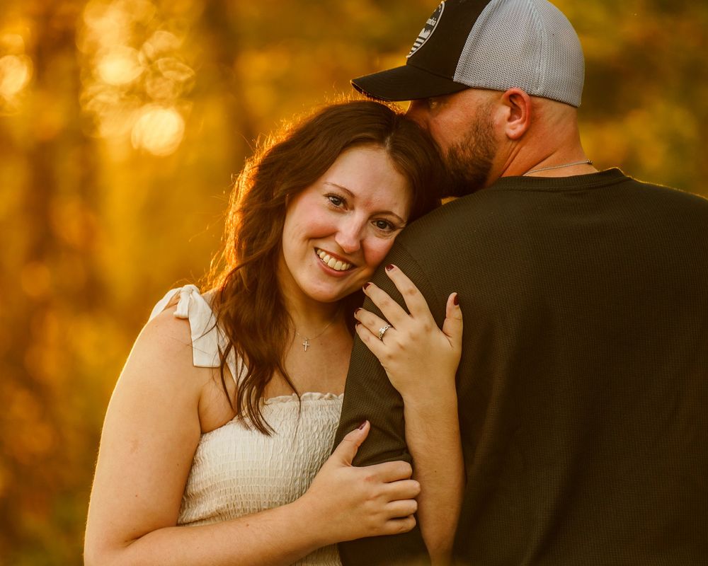 Loving couple embraces during golden hour photo session in autumn setting with warm orange sunlight glowing behind them.