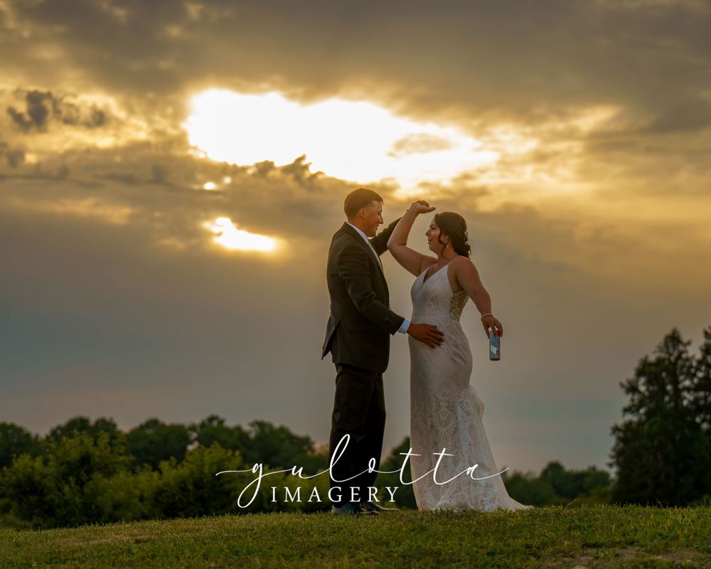 A dancing couple in formal attire silhouetted against a dramatic golden sunset sky with trees on the horizon.