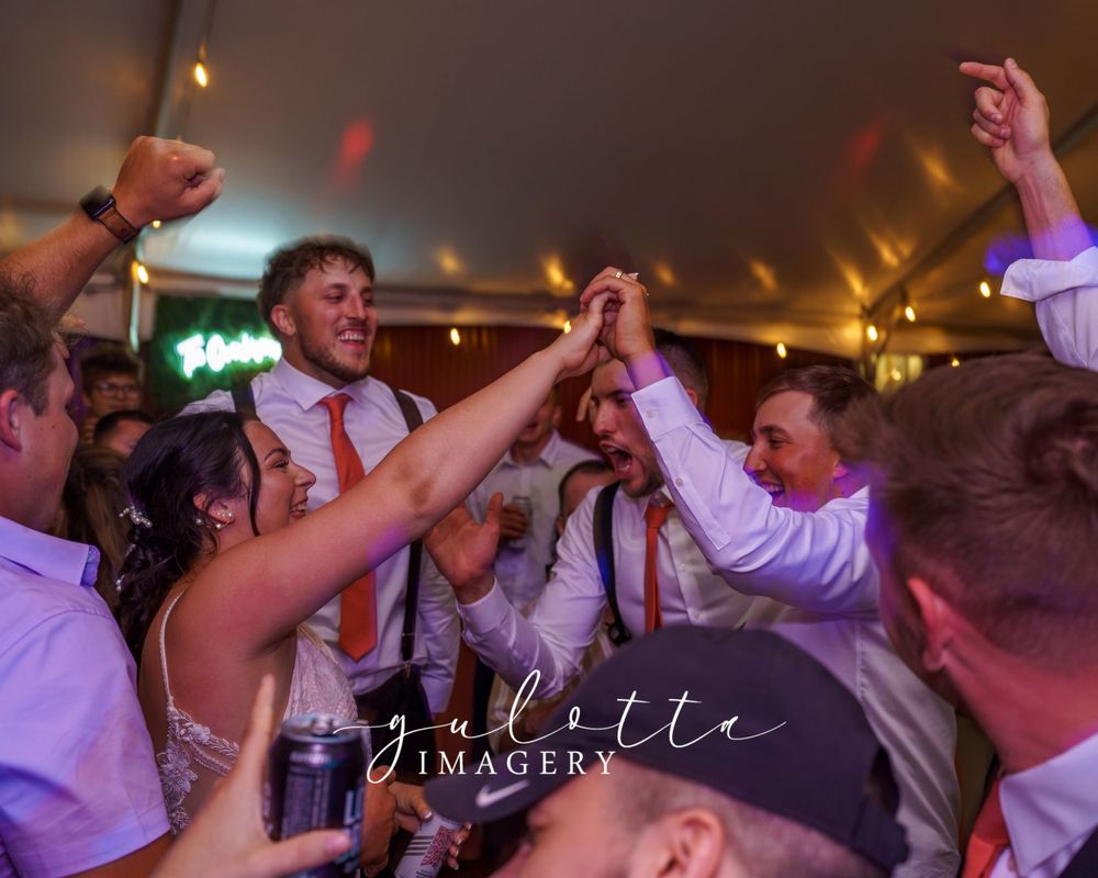 Wedding guests dance and celebrate together on a lively dance floor under warm lighting at an evening reception.