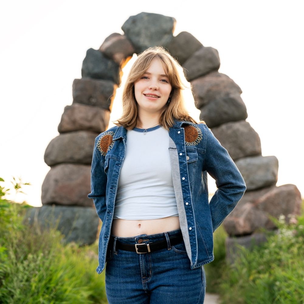Senior photo of girl smiling in front of a brightly lit stone archway, shot by senior photography Rachel Dickman.