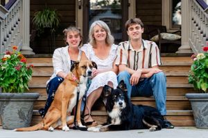 Portrait of family of 3 with 2 dogs smiling, seated on their front steps - shot by Milwaukee family photographer Rachel Dickman.