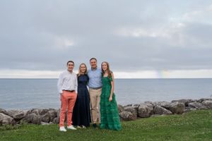 Portrait of family of 4 smiling, standing in front of stones and ocean backdrop - shot by Milwaukee family photographer Rachel Dickman.