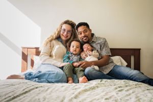 Portrait of mom and dad smiling on a bed with their baby son and newborn infant - shot by Milwaukee Family photographer Rachel Dickman.